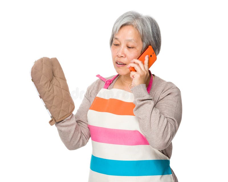 Asiatiskt gammalt hemmafrusamtal till mobiltelefonen med ugnshandsken royaltyfri bild