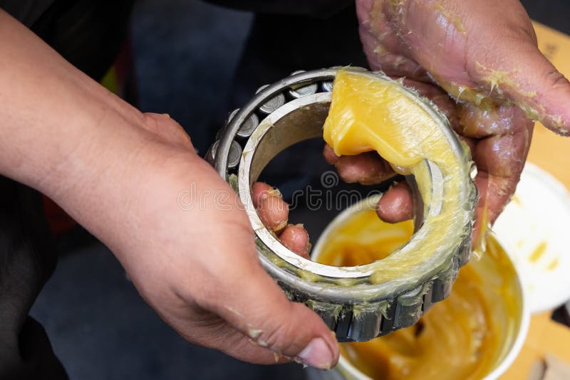 An Asia man putting lithium grease EP extreme pressure NLGI 3 into wheel bearing for ten wheel track by hand in the garage. Industrial and automotive concept. An Asia man putting lithium grease EP extreme pressure NLGI 3 into wheel bearing for ten wheel track by hand in the garage. Industrial and automotive concept