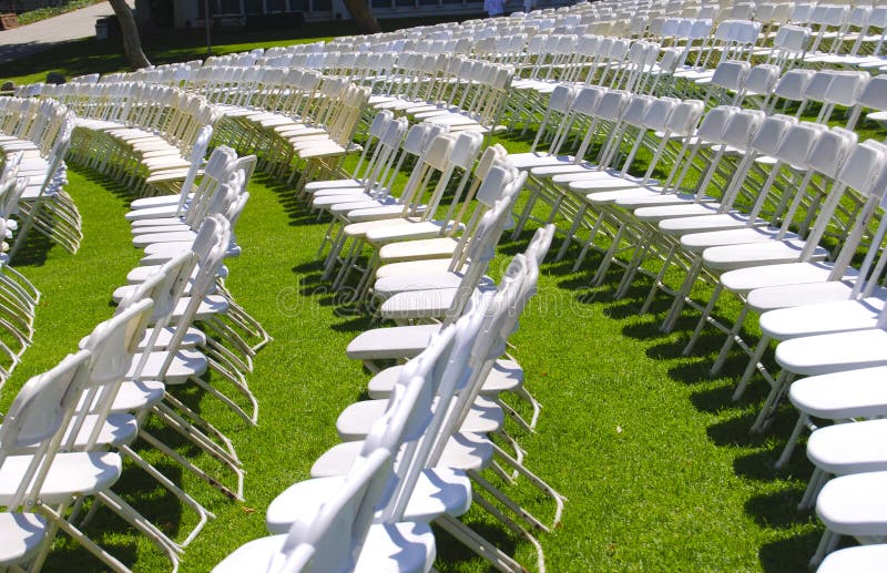 Rows of white folding chairs arranged for a graduation ceremony on a grass lawn. Rows of white folding chairs arranged for a graduation ceremony on a grass lawn.