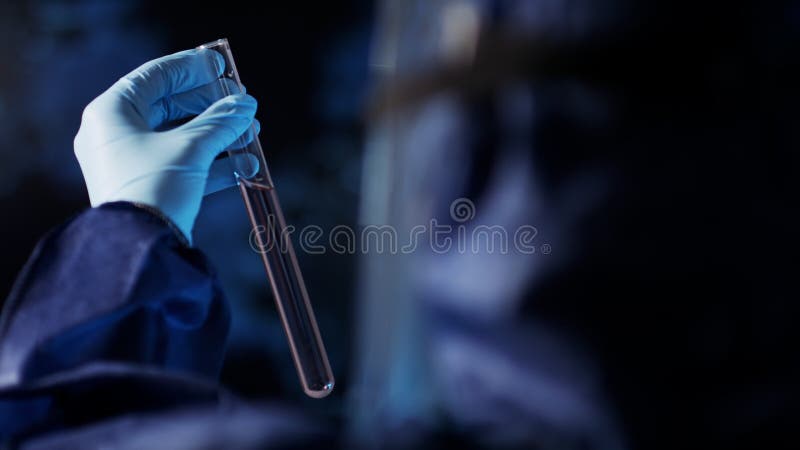 Asistente de laboratorio con traje protector estudiando la muestra en cubeta de tubo de vidrio de laboratorio. foco selectivo de c
