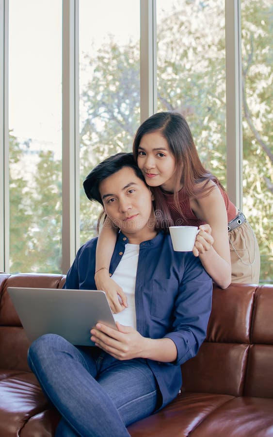 Asiática hermosa mujer sonriendo sosteniendo taza de café abrazando servir a su amigo niño mientras que el uso de la computadora p imagenes de archivo
