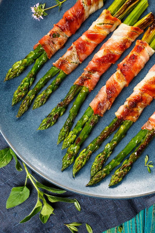 Asperge verte grillée enveloppée avec le lard du plat bleu image libre de droits Asperge verte grillée enveloppée avec le lard du plat bleu image libre de droits