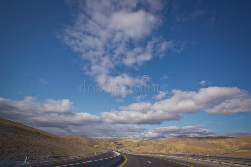 Open road with blue clouds. Asphalt road and bright blue sky with fluffy clouds. Empty desert asphalt road from low angle with mountains and clouds on background. road, red desert landscape