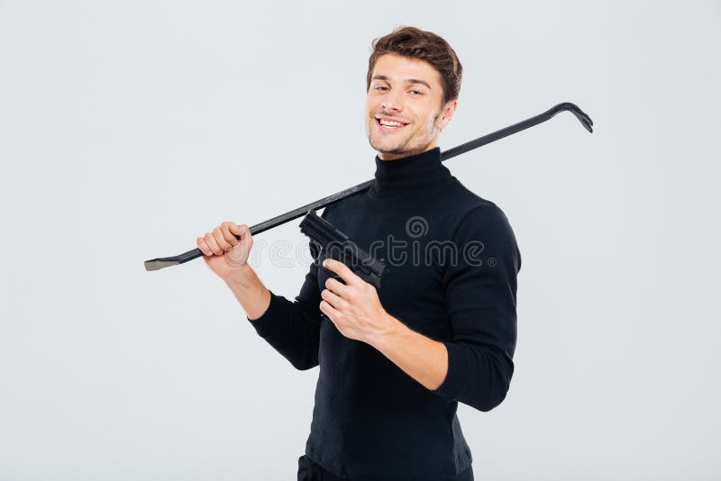 Assaltante criminoso de sorriso que está com arma e pé de cabra fotografia de stock royalty free Assaltante criminoso de sorriso que está com arma e pé de cabra fotografia de stock royalty free