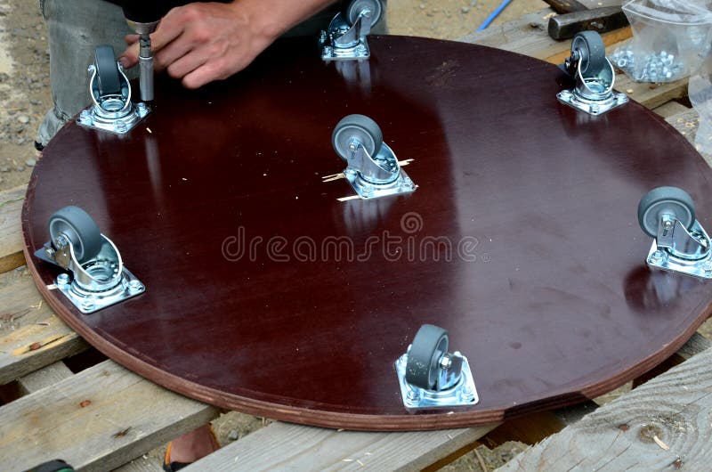 Assembly of industrial swivel castors on a wooden board made of brown plywood. It serves as a moving trolley for transporting heav