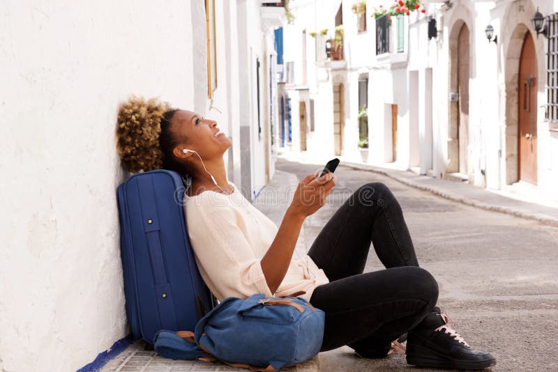 Assento fêmea do viajante afro-americano no passeio e música de escuta do telefone esperto