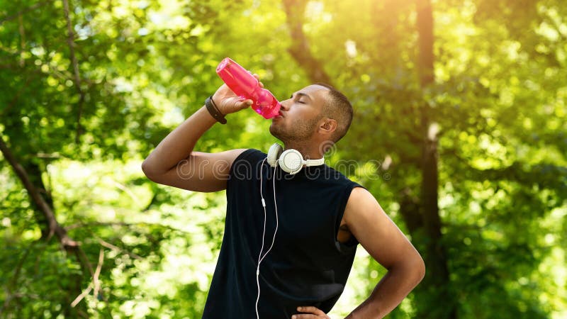 Assetato giovane atleta che beve acqua dalla bottiglia dopo il suo allenamento a Park immagine stock libera da diritti