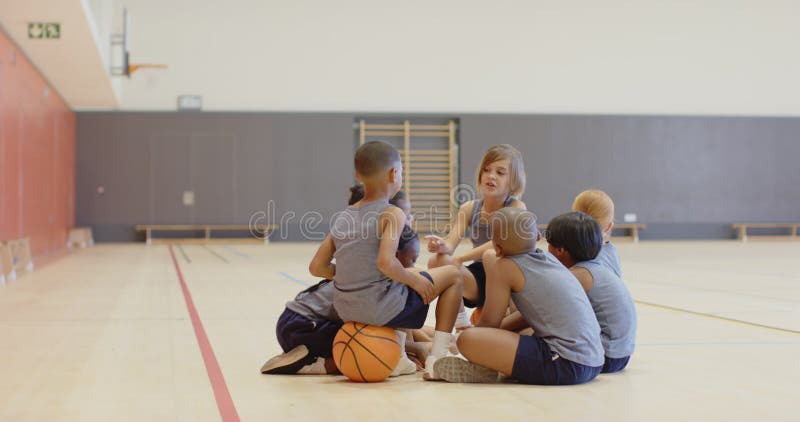 Assis dans le groupe d'enfants d'école de gym parlant avec le basket-ball à l'étage banque de vidéos