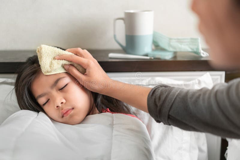 Asian mother take cool towel for reduce high fever on sick girl forehead on bed at morning time, Selective focus, Healthy and infection concept. Asian mother take cool towel for reduce high fever on sick girl forehead on bed at morning time, Selective focus, Healthy and infection concept.