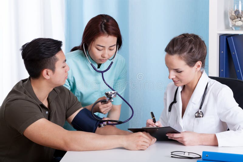 Assistant féminin asiatique prenant la tension artérielle du patient masculin photos stock Assistant féminin asiatique prenant la tension artérielle du patient masculin photos stock