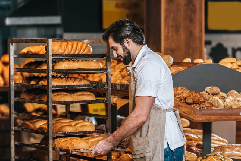 assistente de loja masculino no avental que arranja a pastelaria fresca imagens de stock assistente de loja masculino no avental que arranja a pastelaria fresca imagens de stock