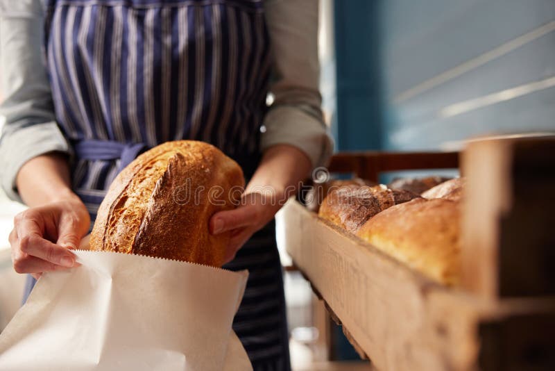 Assistente de vendas em padaria colocando pão de pão de pasta de origem orgânica recém-cozida em saco de papel sustentável