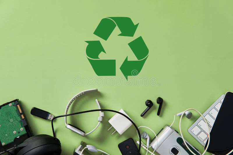 Assorted electronic waste and obsolete gadgets clustered below a prominent green recycling symbol on stock photo