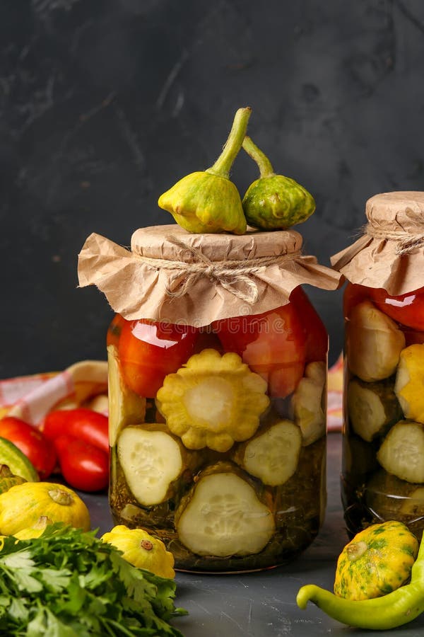 Assorted pickled cucumbers, patissons and tomatoes in jars on a dark background, vertical orientation stock photo Assorted pickled cucumbers, patissons and tomatoes in jars on a dark background, vertical orientation stock photo