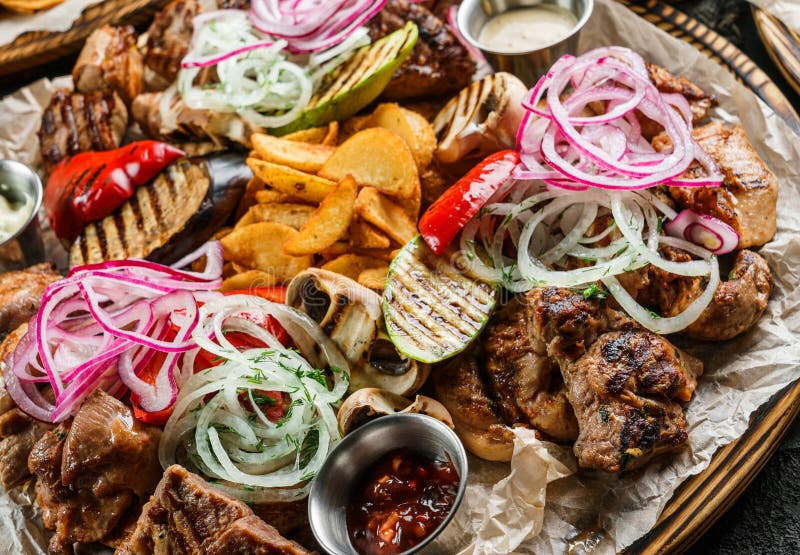 Assorted snacks for beer in plates, delicious grilled meat, vegetables, fries potatoes, bbq sauce and beer in glass on dark