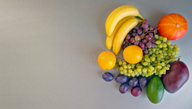 Assortimento colorato di frutta con zucca su fondo grigio. Un'esposizione vibrante di frutta fresca, comprese le uve di banana fotografia stock