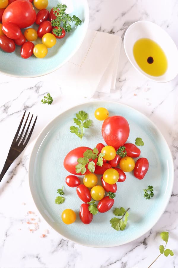 Assortimento dei pomodori ciliegia rossi e gialli su un piatto, su un coriandolo e su un olio d'oliva blu fotografia stock libera da diritti Assortimento dei pomodori ciliegia rossi e gialli su un piatto, su un coriandolo e su un olio d'oliva blu fotografia stock libera da diritti