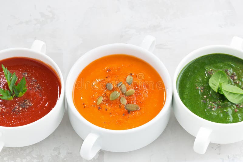 Assortment of colorful vegetable cream soup on white background