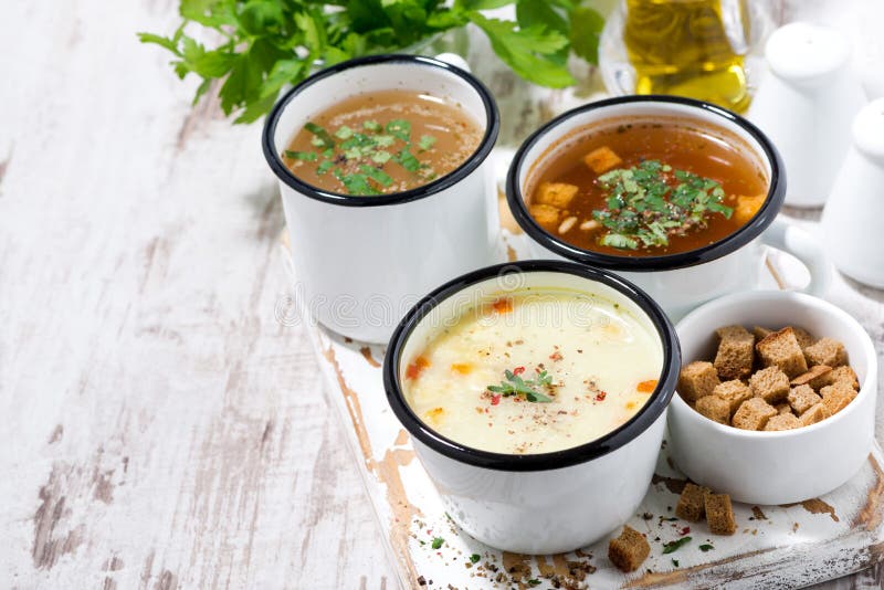 Assortment of hot soups in mugs on wooden background