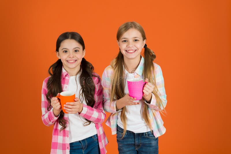 Assurez-vous que les enfants boivent assez d'eau Les enfants de filles tiennent le fond orange de tasses Les soeurs tiennent des photos stock Assurez-vous que les enfants boivent assez d'eau Les enfants de filles tiennent le fond orange de tasses Les soeurs tiennent des photos stock