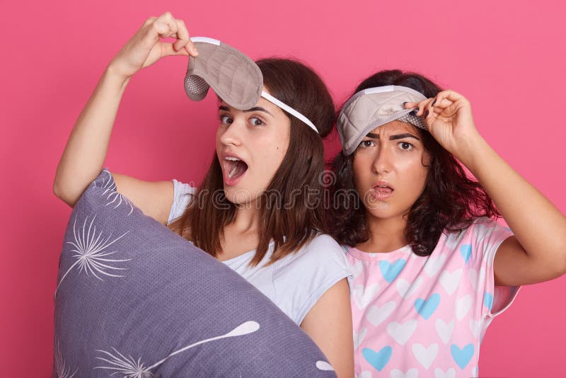 Astonished females dress sleeping mask posing with opened mouths indoor, lady with straight hair holding grey pillow in hands, stock image Astonished females dress sleeping mask posing with opened mouths indoor, lady with straight hair holding grey pillow in hands, stock image