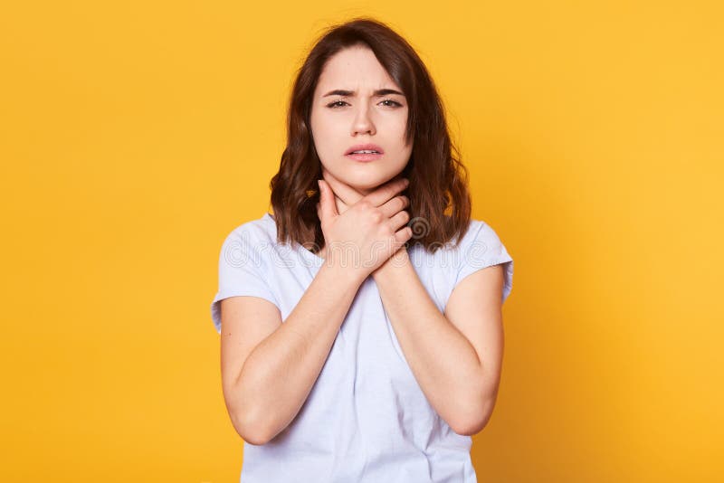 Atelieraufnahme der angenehmen schauenden Frau mit umgekipptem Blick, trägt weißes zufälliges T-Shirt, hält beide Hände auf Hals, lizenzfreies stockbild Atelieraufnahme der angenehmen schauenden Frau mit umgekipptem Blick, trägt weißes zufälliges T-Shirt, hält beide Hände auf Hals, lizenzfreies stockbild
