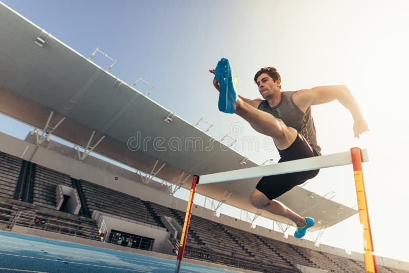 Athlete jumping over an hurdle on running track