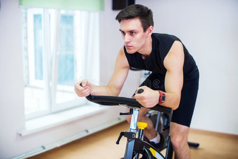 Athlete man biking in the gym, exercising his legs doing cardio training cycling bikes
