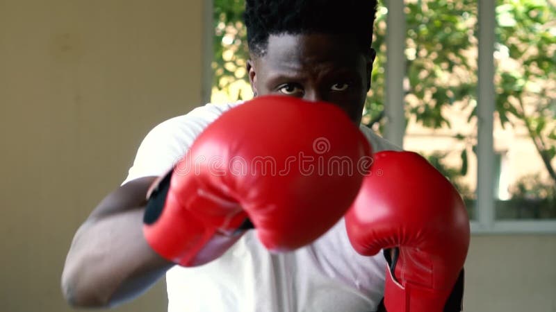 Athletic African American sportsman in red boxing gloves attacking during workout. Male boxer punching in gym
