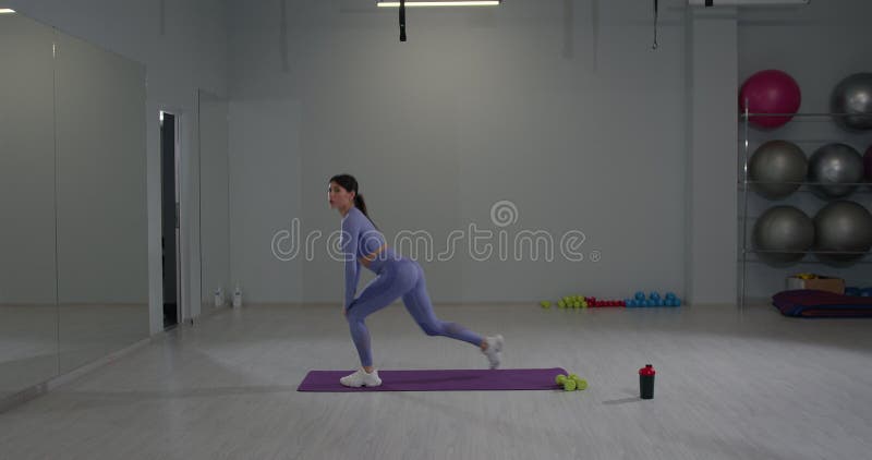 Athletic girl exécutant des poumons avant pour s'étirer dans une salle de gym moderne pendant la journée banque de vidéos