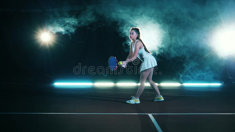 Athletic lady está sirviendo una pelota de tenis en un salón oscuro