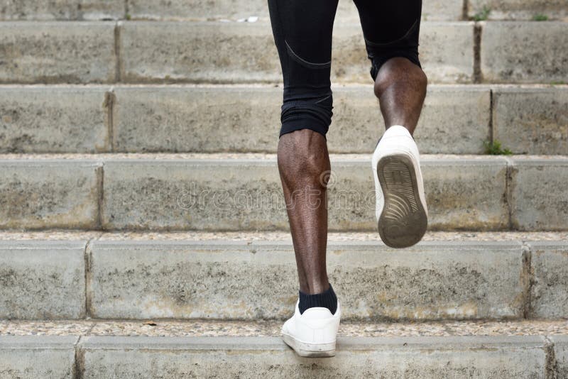 Athletic legs of black man running on staircase steps.