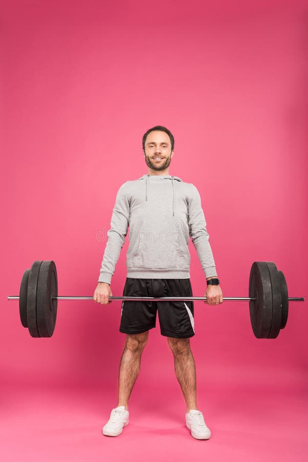 athletic man in sportswear training with barbell, isolated on pink