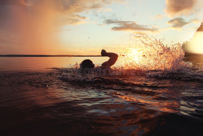 Athletic man is trained to swim in a lake at sunset. It flies a lot of water splashing