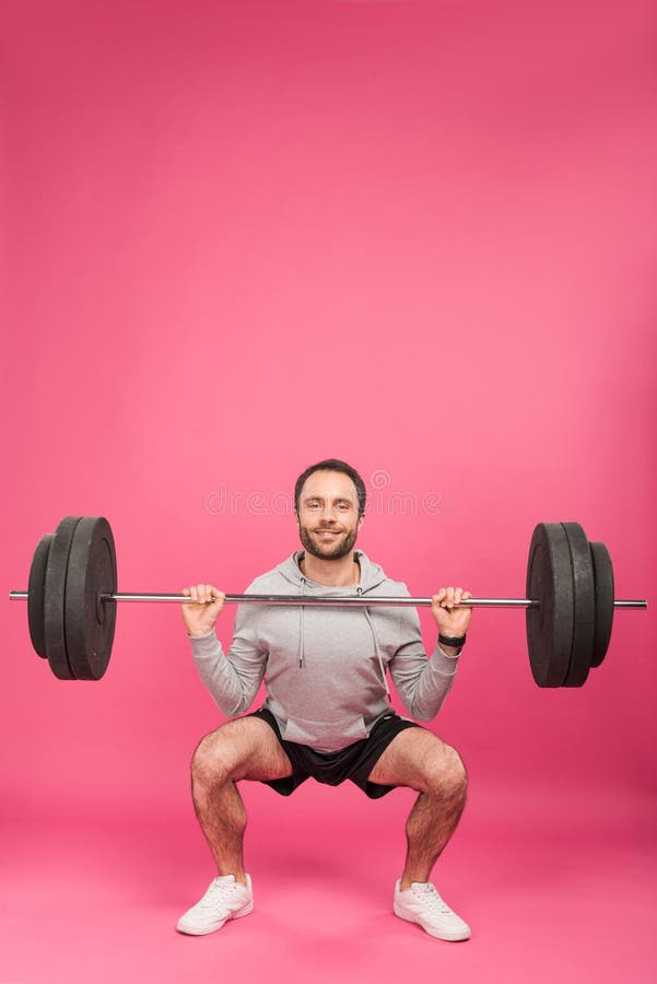 athletic man training with barbell, isolated on pink