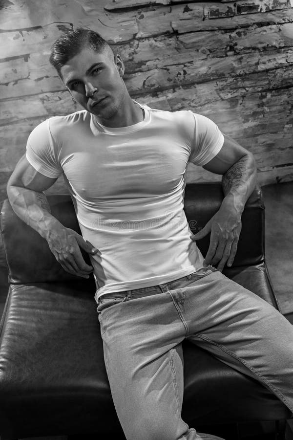 Athletic man in white t-shirt tight sexy abs sitting on a leather sofa