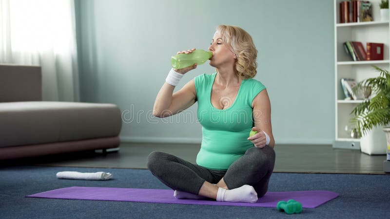 Athletic senior woman sitting on floor and drinking water after workout, health stock photos Athletic senior woman sitting on floor and drinking water after workout, health stock photos