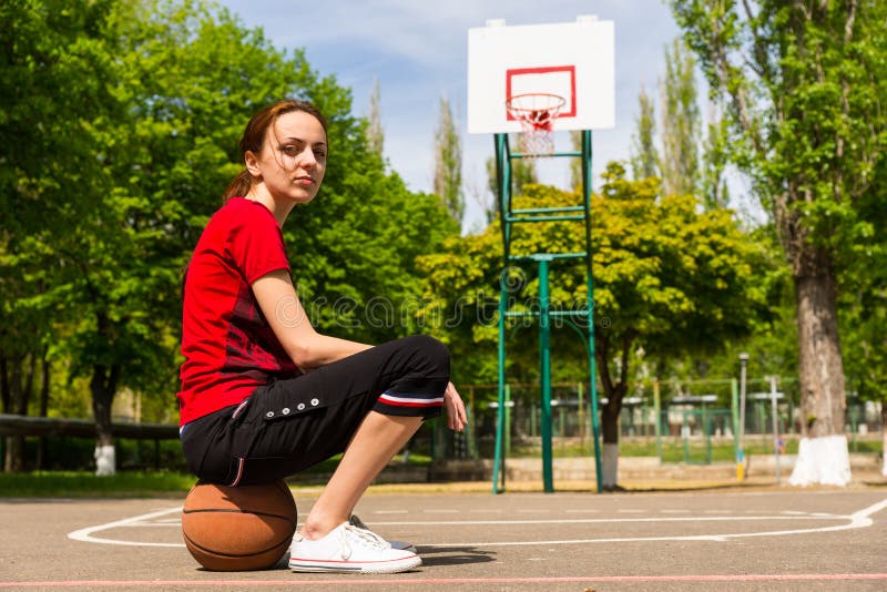 Athletic Woman Sitting on Basketball on Court