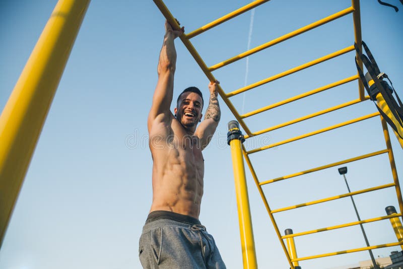 Athletic young man hanging from the bars at the calisthenics gym outdoors