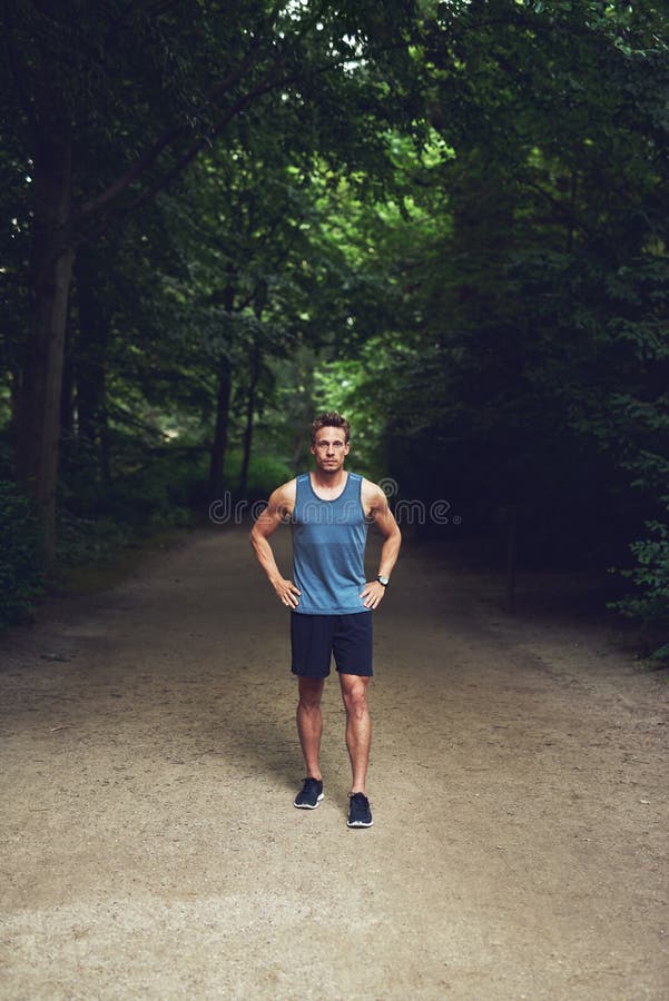 Athletic young man in sportswear standing waiting in a park with his hands on his hips looking up at the camera, high angle full length view. Athletic young man in sportswear standing waiting in a park with his hands on his hips looking up at the camera, high angle full length view