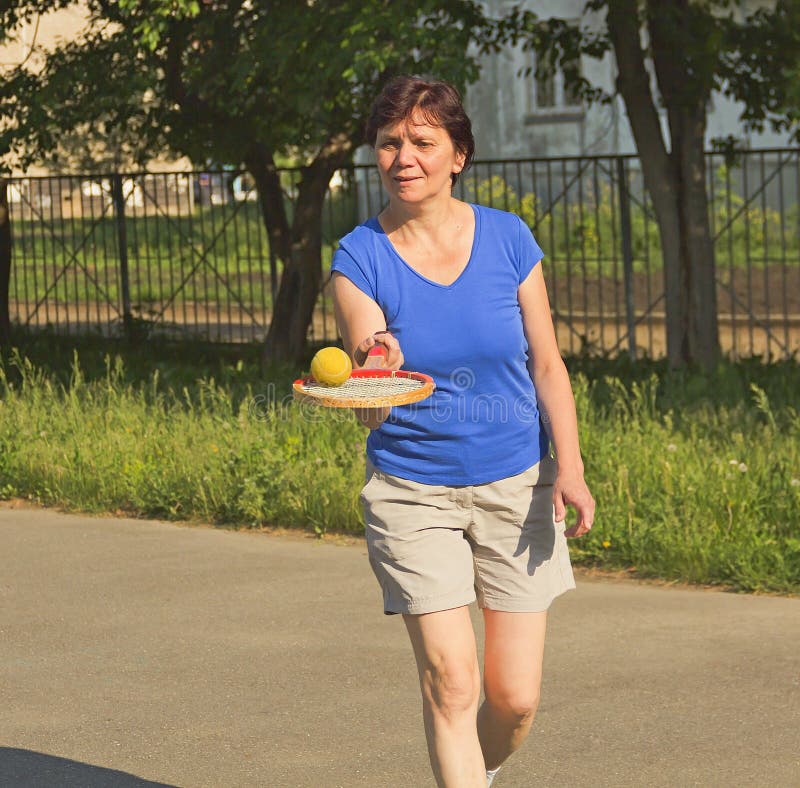 Athletische ältere Frau, die einen Tennisball anfüllt lizenzfreie stockfotografie Athletische ältere Frau, die einen Tennisball anfüllt lizenzfreie stockfotografie