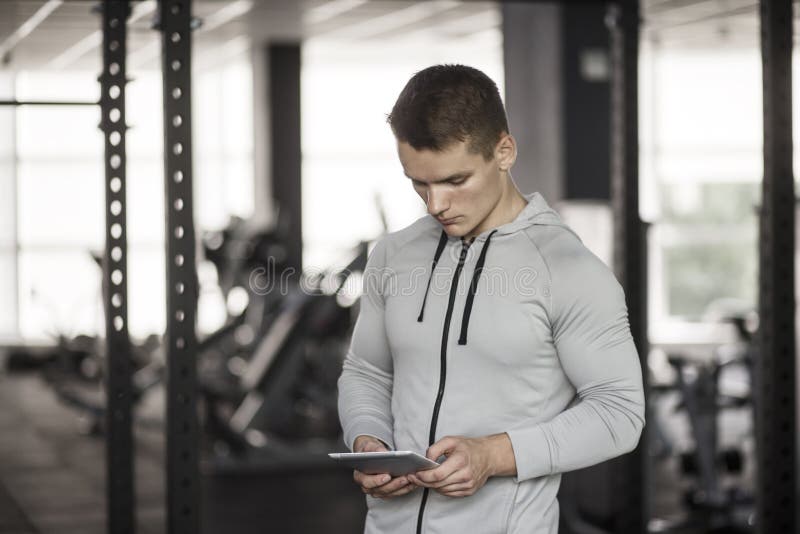 Athletischer junger Mann auf digitaler Tablette vor der Ausbildung an der Turnhalle, unter Verwendung der Anwendung mit Trainings stockfoto Athletischer junger Mann auf digitaler Tablette vor der Ausbildung an der Turnhalle, unter Verwendung der Anwendung mit Trainings stockfoto