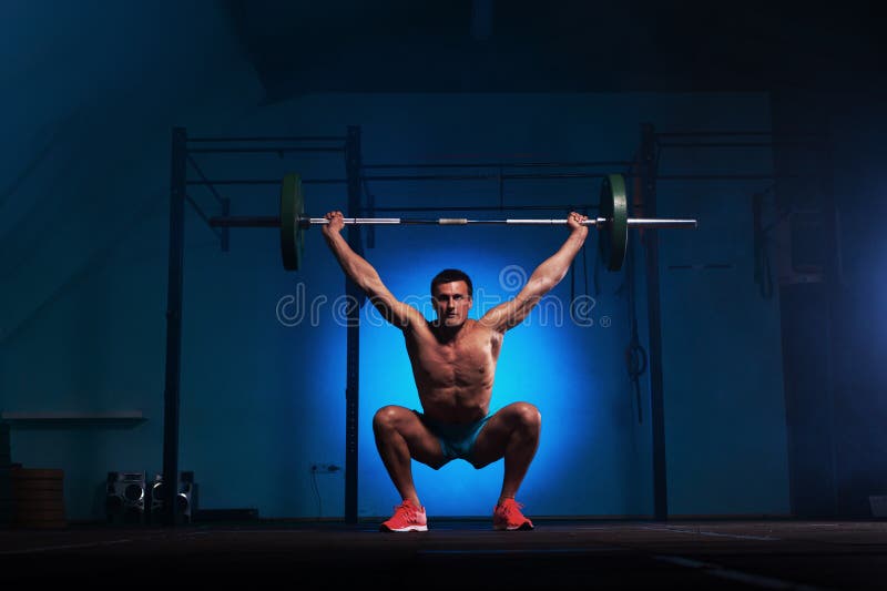 Athletischer junger Mann, der mit Barbell in der Turnhalle ausarbeitet lizenzfreies stockbild Athletischer junger Mann, der mit Barbell in der Turnhalle ausarbeitet lizenzfreies stockbild