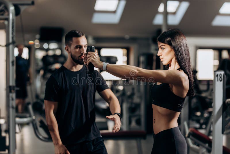 Athletisches Mädchen, das Übung für die Muskeln der Arme mit Gewicht in der Turnhalle unter Aufsicht eines Trainers tut stockfoto