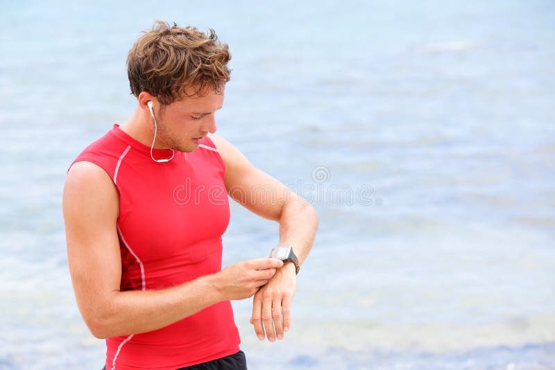 Athlete runner looking at heart rate monitor watch. Man running on beach taking a break in compression t-shirt top. Athlete runner looking at heart rate monitor watch. Man running on beach taking a break in compression t-shirt top.