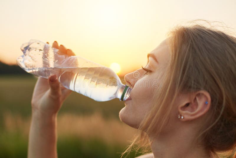 Atleta de sexo femenino que tiene sed después de correr, sosteniendo la botella plástica, agua fría de consumición, descansando d imágenes de archivo libres de regalías Atleta de sexo femenino que tiene sed después de correr, sosteniendo la botella plástica, agua fría de consumición, descansando d imágenes de archivo libres de regalías