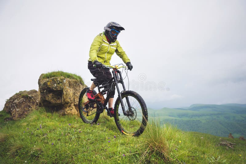 Atleta de sexo masculino envejecido en paseos del casco y de la máscara abajo de una cuesta herbosa en una bici de montaña Concep fotos de archivo libres de regalías Atleta de sexo masculino envejecido en paseos del casco y de la máscara abajo de una cuesta herbosa en una bici de montaña Concep fotos de archivo libres de regalías
