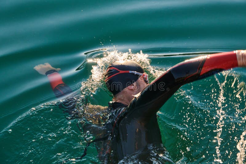 Atleta de triatlón nadando en el lago al amanecer usando traje húmedo imagen de archivo libre de regalías