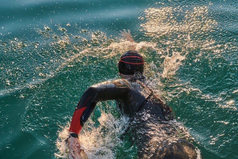 Atleta de triatlón nadando en el lago al amanecer usando traje húmedo imagen de archivo libre de regalías