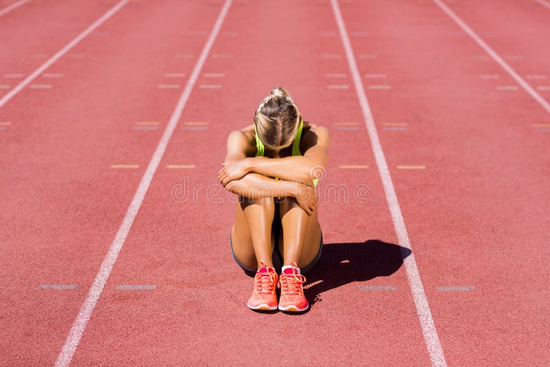 Atleta fêmea virado que senta-se na pista de atletismo